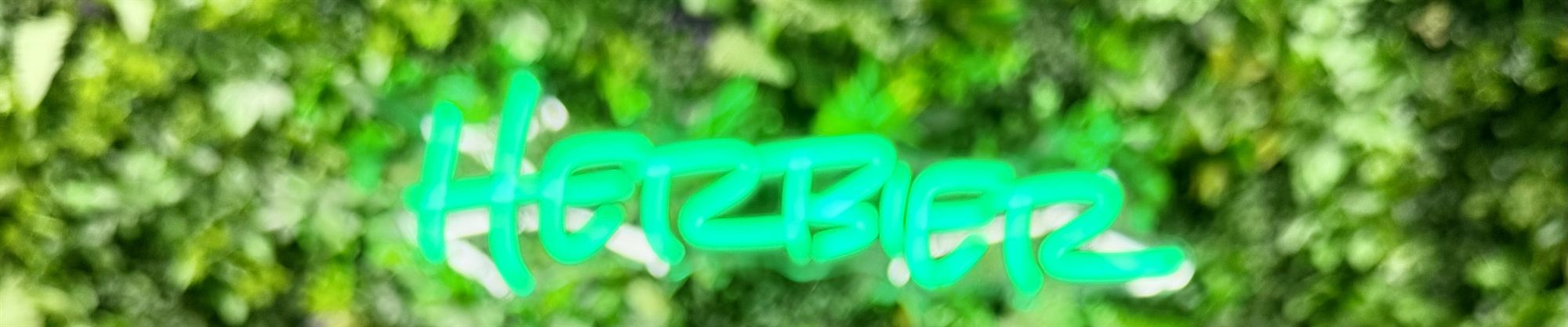 The Herbiez neon sign glowing on the living plant wall inside our Omaha shop